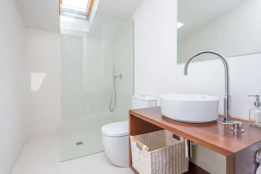 Un baño luminoso con ducha de vidrio, lavabo sobre encimera y tocador de madera.