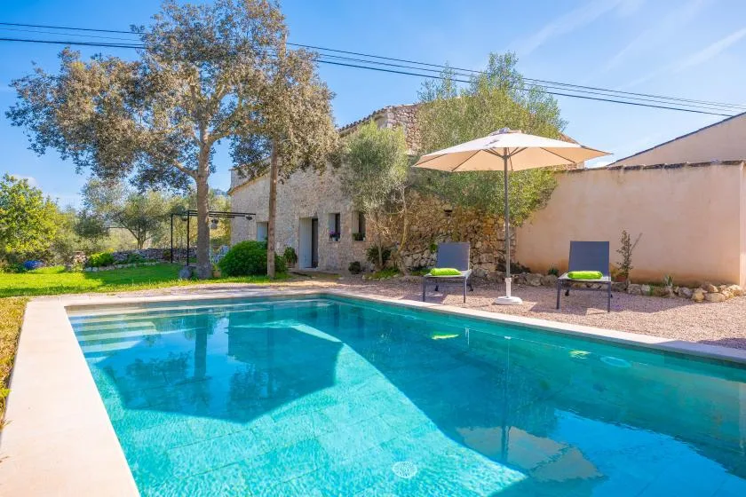 Una piscina está junto a un edificio de piedra, con una sombrilla y asientos cerca.