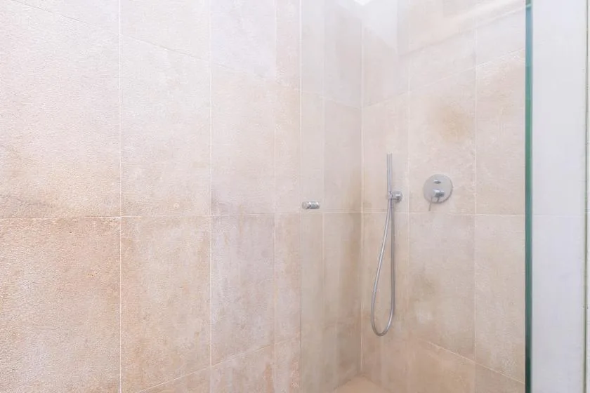 Una ducha alicatada con una ducha de mano y controles en la pared.