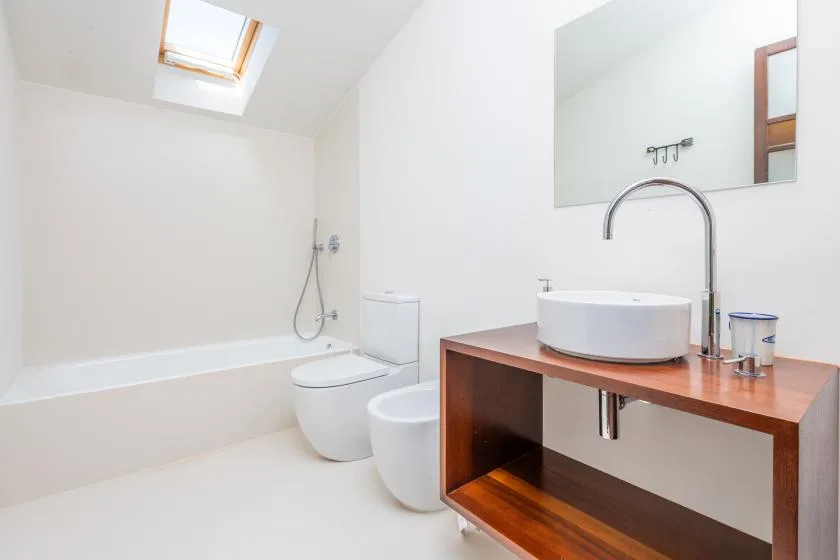 Un baño luminoso con bañera, inodoro y lavabo sobre un mueble de madera.