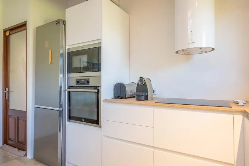 Una cocina moderna con refrigerador, horno empotrado y pequeños electrodomésticos sobre la encimera.