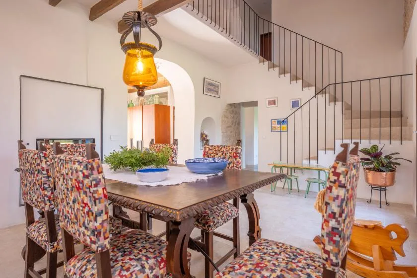 Comedor con una mesa larga y asientos estampados bajo una escalera.