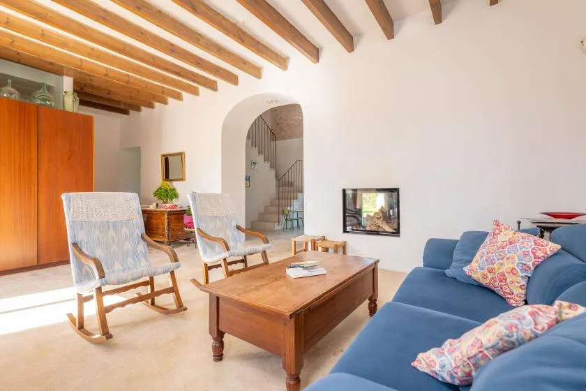 Una sala de estar con asientos azules, sillas de madera y una mesa de centro bajo vigas vistas.