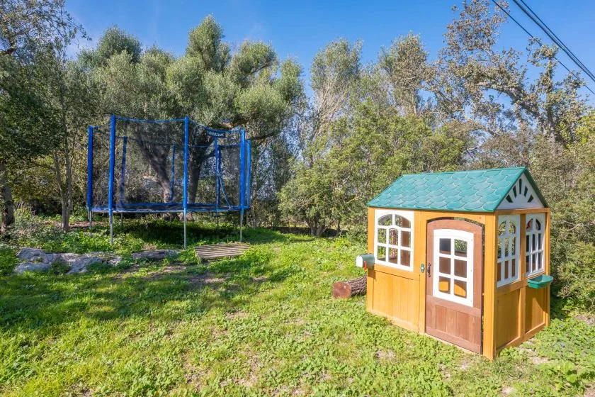 Una zona de juegos al aire libre con césped tiene un trampolín y una casita de juegos.