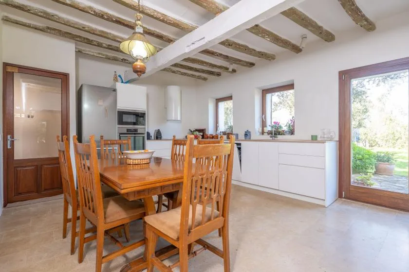 Comedor con una mesa y sillas de madera junto a una cocina blanca.