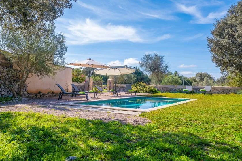 Una piscina al aire libre está junto a un césped y una zona de descanso con sombra.