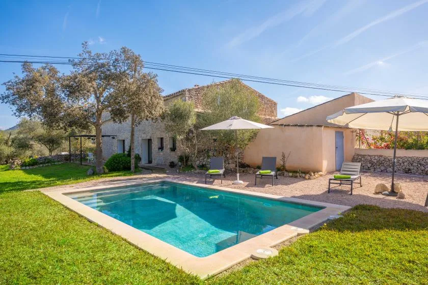 Una piscina al aire libre está junto a un patio ajardinado con asientos y sombrillas.