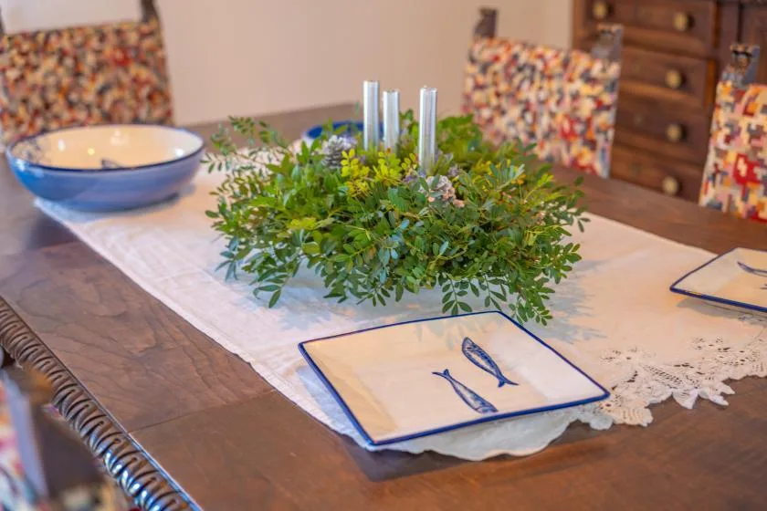 Una mesa de comedor está preparada con un centro de hojas y vajilla.
