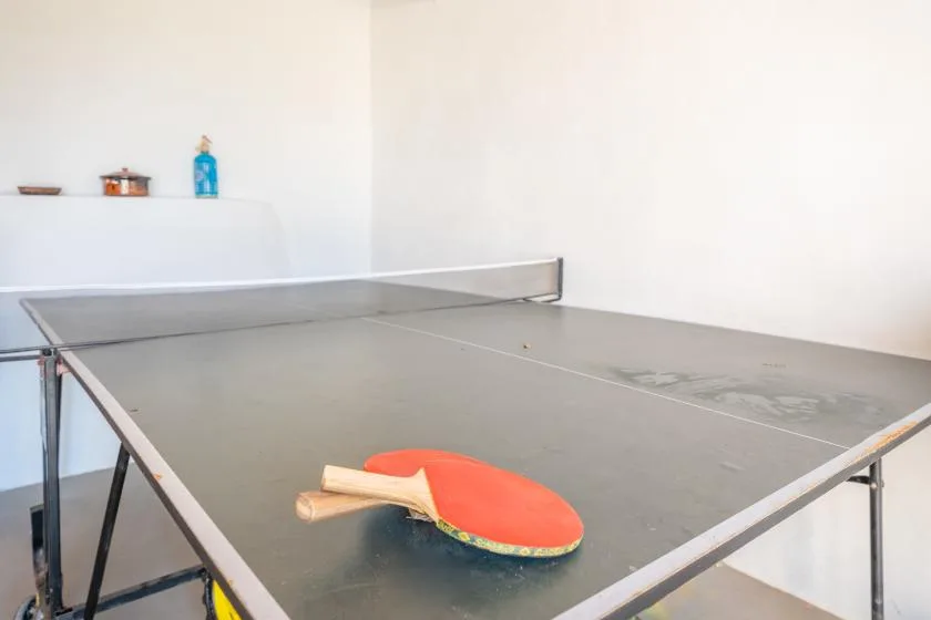 Una mesa de ping-pong con una paleta está en una habitación luminosa y poco decorada.