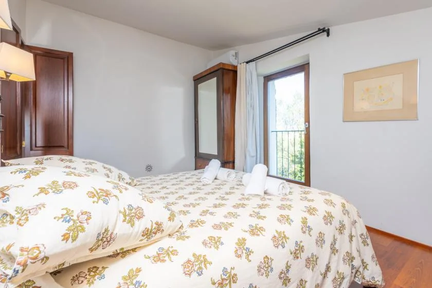 Un dormitorio con ropa de cama floral, un armario con espejo y una puerta acristalada que da a un balcón.