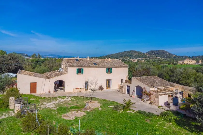 Una casa de estuco claro y una construcción anexa se alzan junto a un patio con césped.