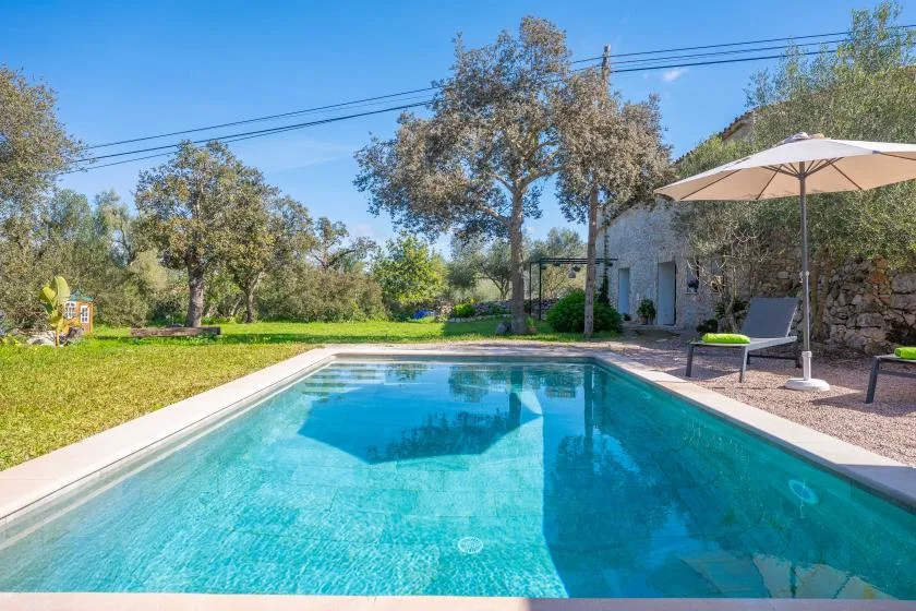 Una piscina al aire libre está junto a un jardín con césped y un edificio de piedra.