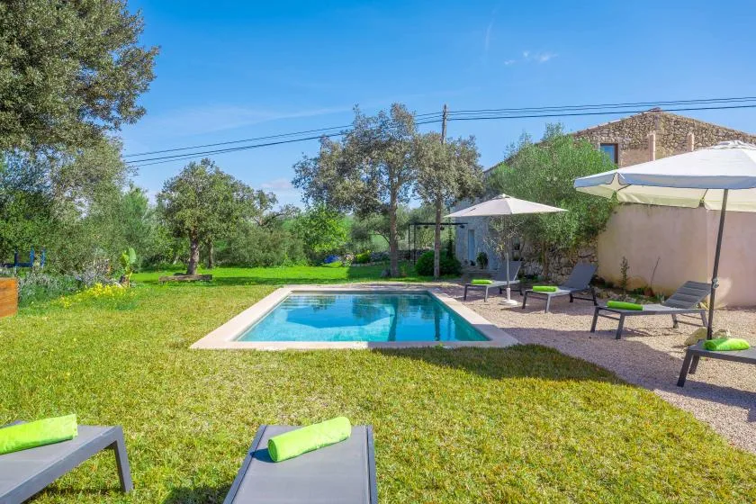 Una piscina está en un jardín al aire libre con césped, tumbonas y sombrillas.