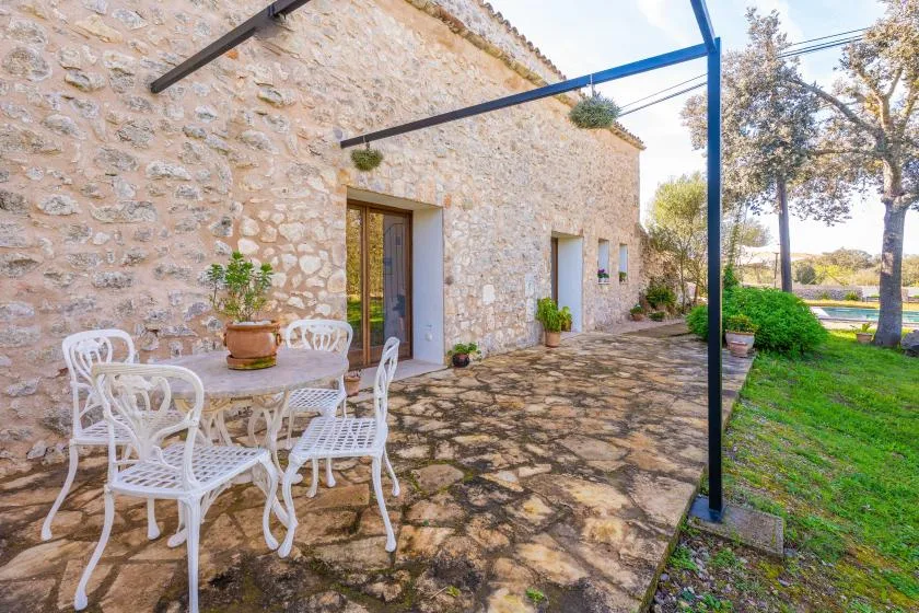 Un edificio de piedra da a un patio pavimentado con asientos al aire libre y vegetación.