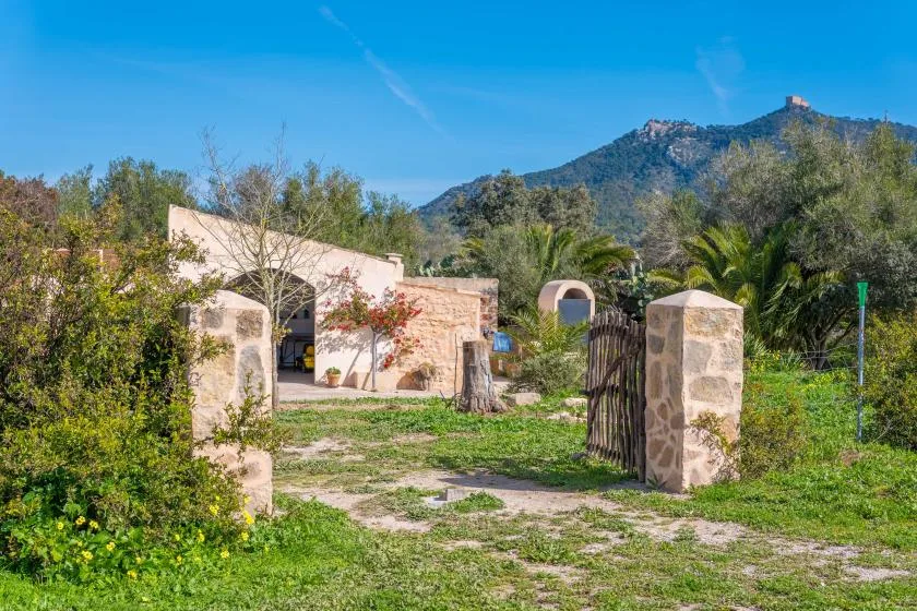 Una entrada ajardinada con pilares de piedra conduce a un edificio bajo, al pie de una montaña.