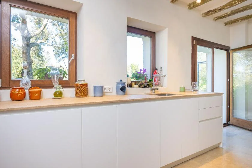 Una cocina luminosa con gabinetes blancos, encimeras de madera y ventanas grandes.