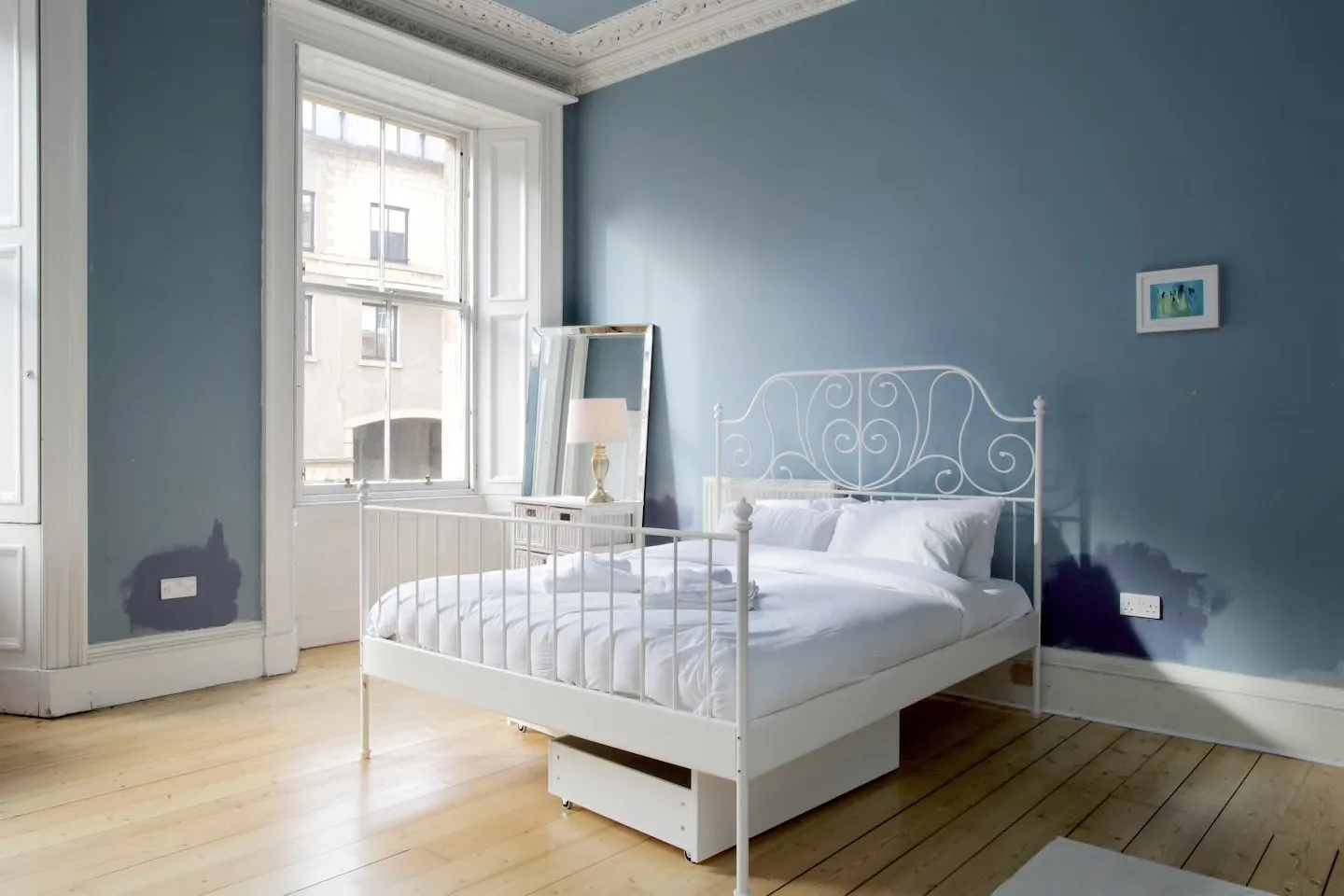 A bright bedroom with a white bed beside a tall window.