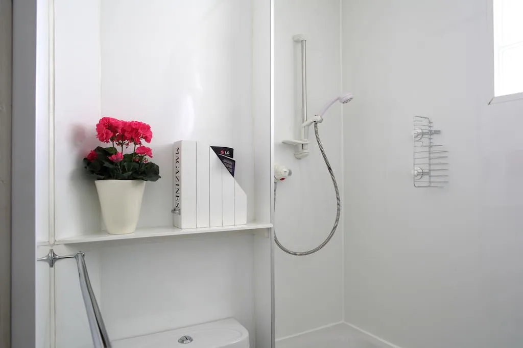 A bright white bathroom with a wall-mounted shower and a small flower arrangement.