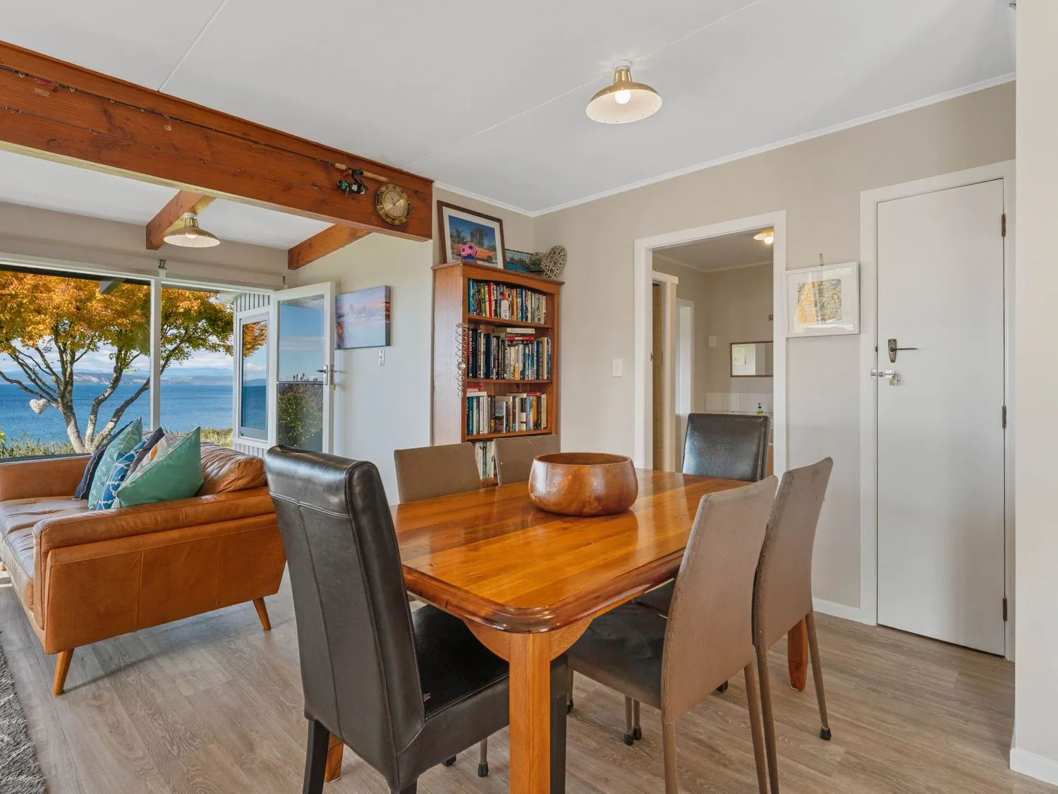 Una zona de comedor y sala de estar con mesa de madera y asientos junto a una ventana abierta.