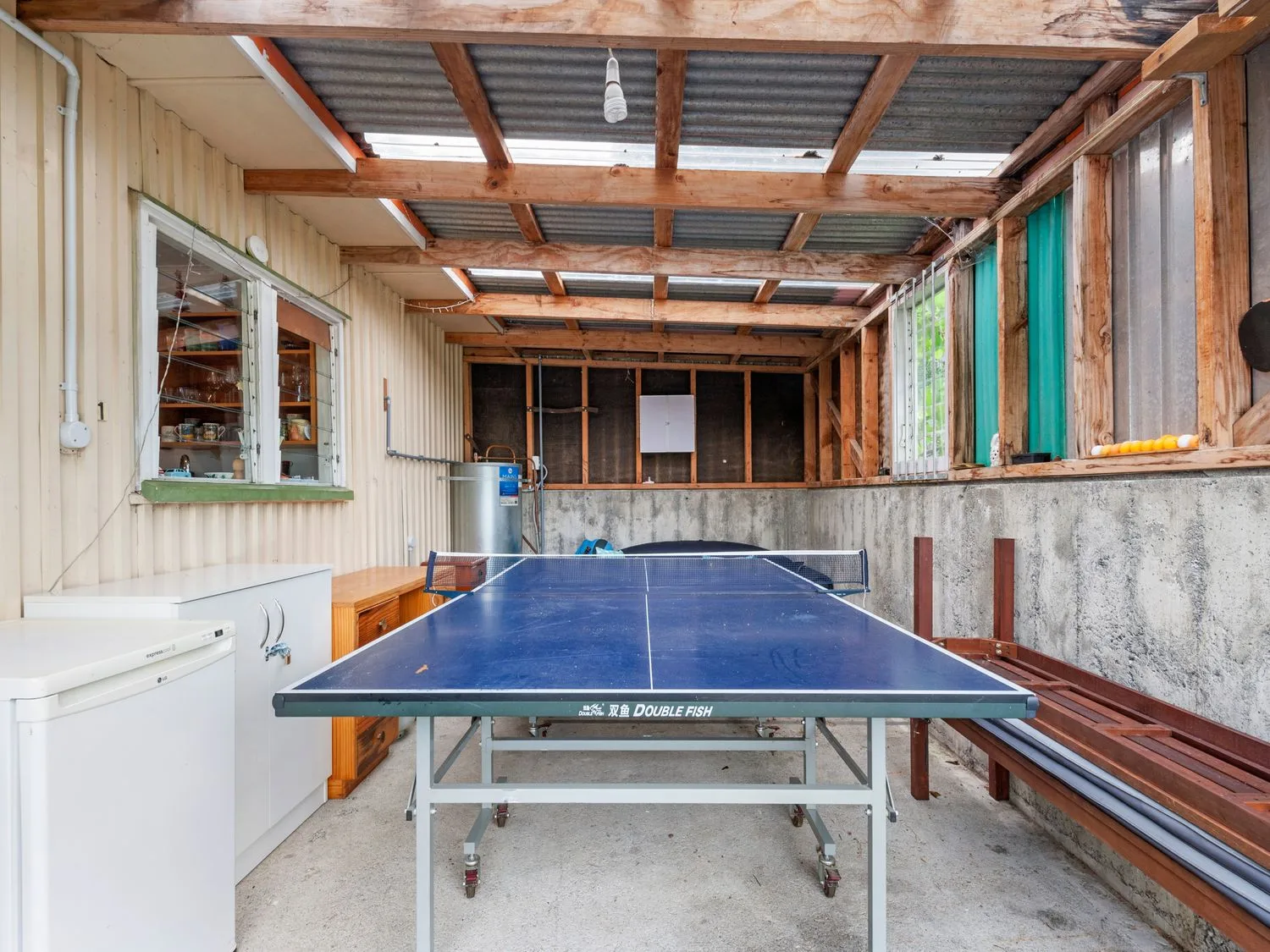 Un espacio exterior cubierto con una mesa de ping-pong, un refrigerador, armarios de almacenamiento y un banco en Henley - Omori Holiday Home, en Omori