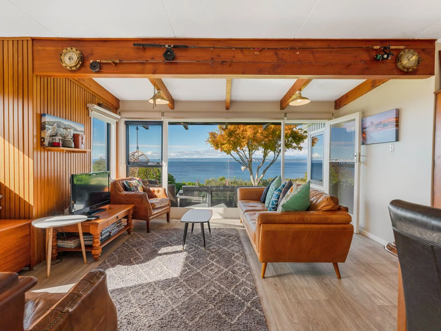 Una sala de estar con sofás de cuero, una mesa de centro, un televisor y grandes ventanas con vistas al mar en Henley - Omori Holiday Home, en Omori