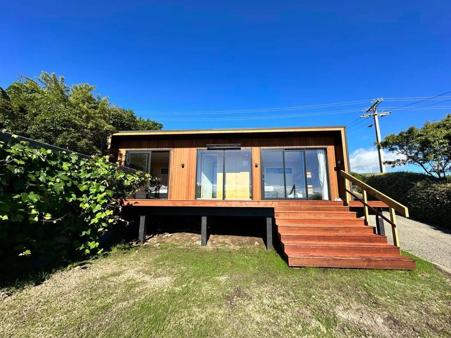 Una casa moderna con puertas de vidrio y escalones de madera, rodeada de vegetación.