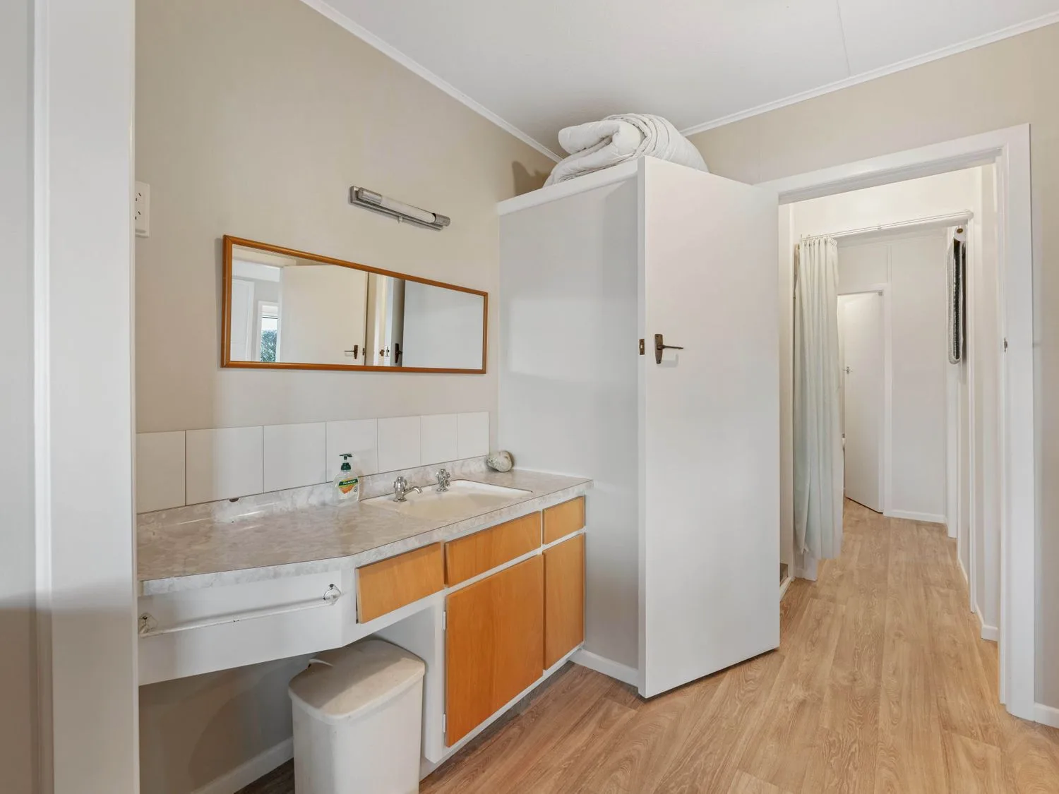 Un baño con una encimera larga con lavabo, un armario con espejo y una puerta abierta al pasillo.