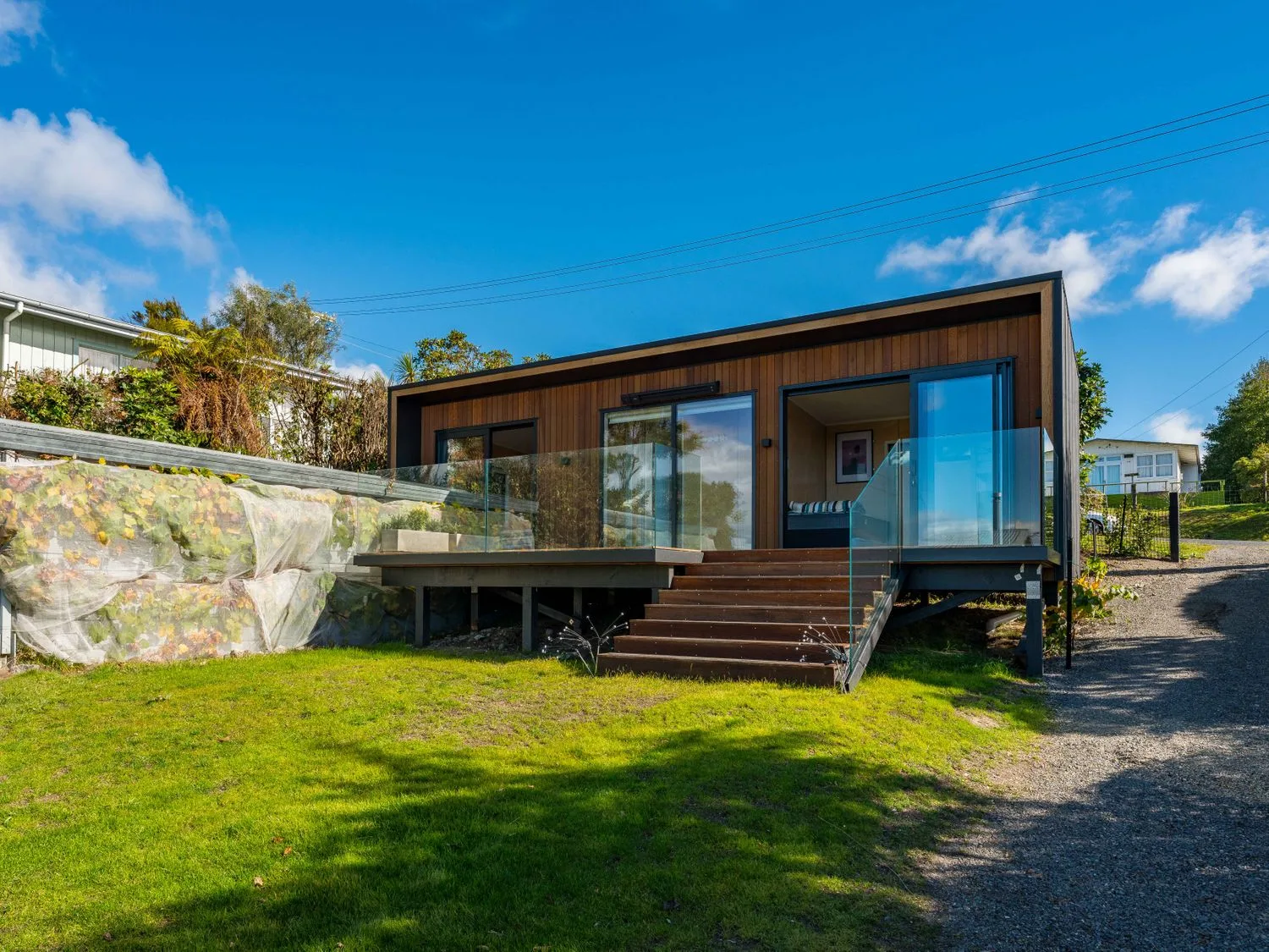 Una casa moderna de una sola planta con una terraza de madera y barandillas de vidrio con vistas a un césped en Henley - Omori Holiday Home, en Omori