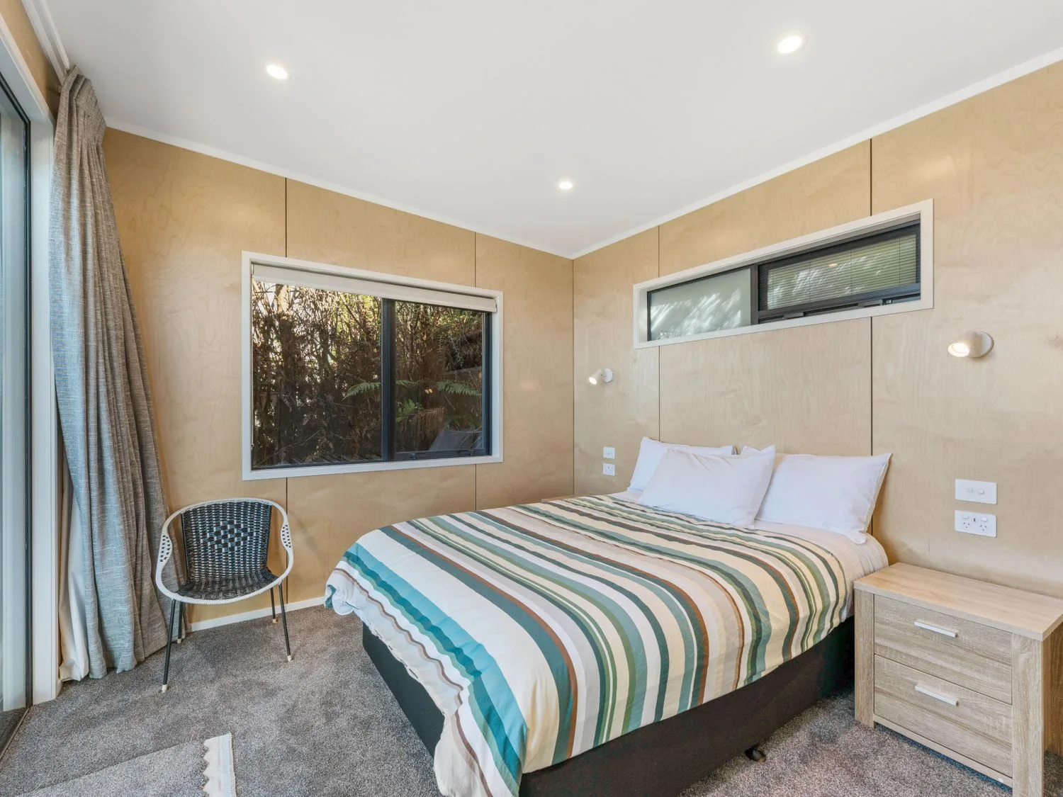 Un dormitorio con una cama con ropa de cama a rayas, una mesa de noche de madera, una silla y dos ventanas en Henley - Omori Holiday Home, en Omori