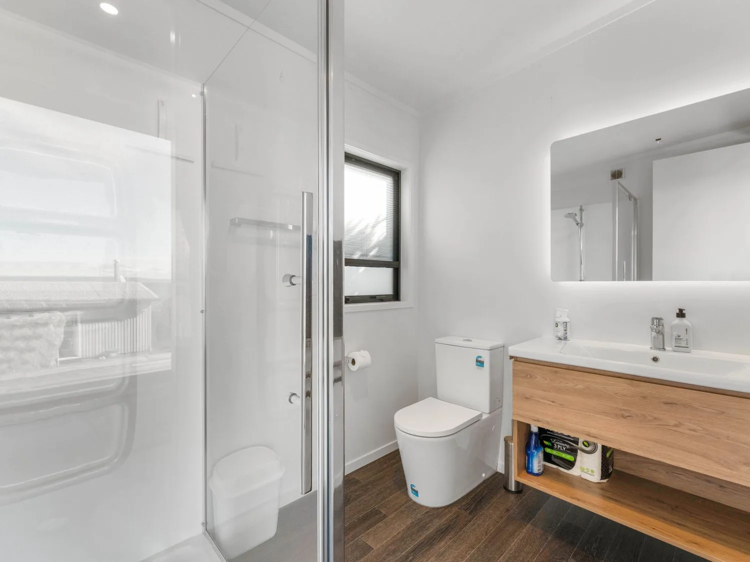 Un baño con ducha, inodoro, mueble de madera y espejo.