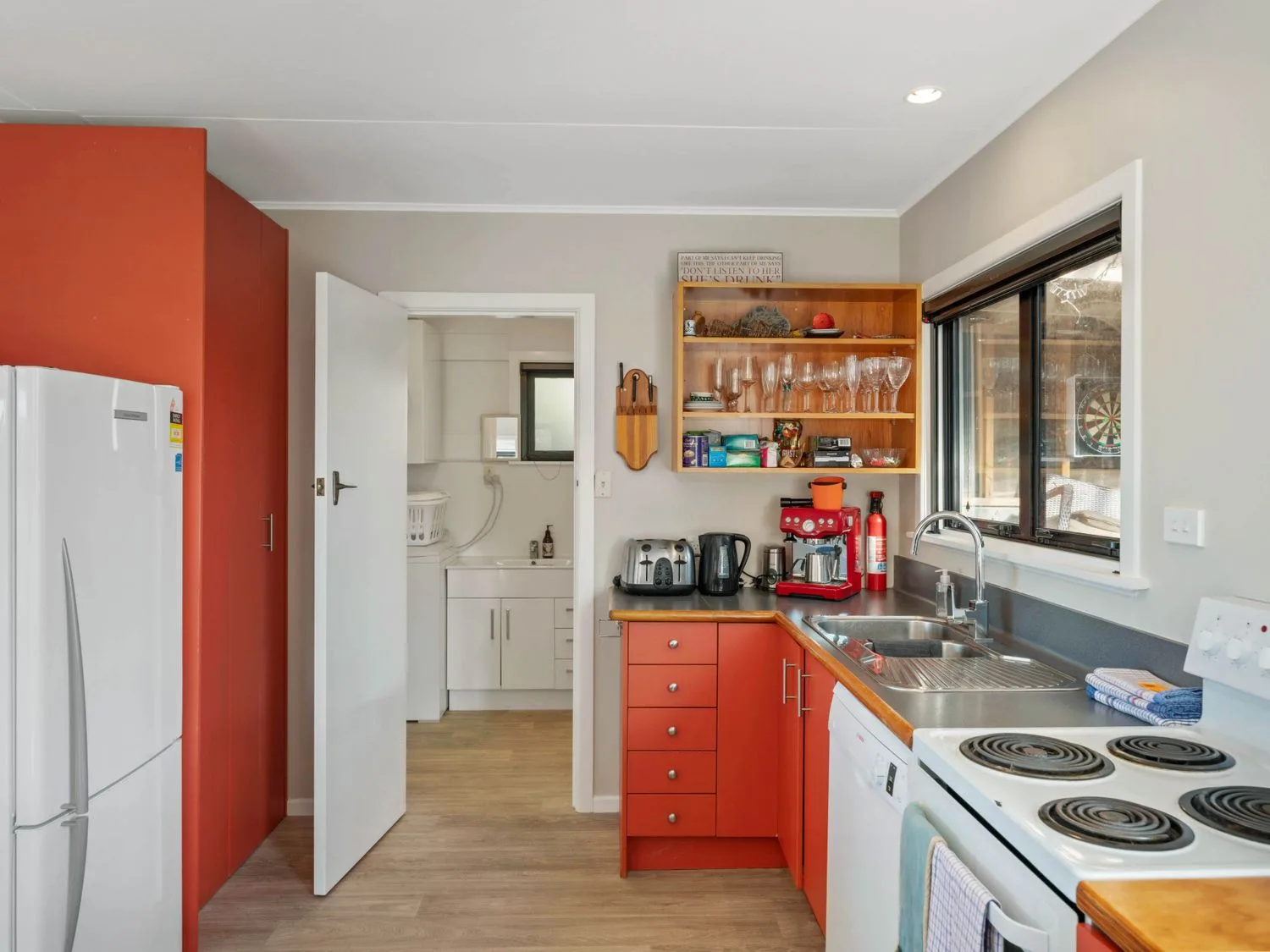 Una cocina con armarios rojos, un refrigerador blanco y un fregadero bajo la ventana.