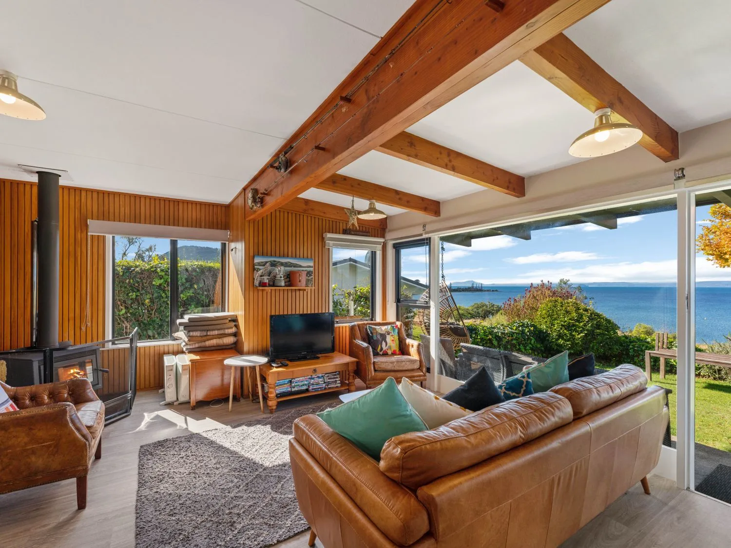 Una sala de estar con sofás de cuero, un televisor, revestimiento de madera, vigas de techo a la vista y vistas al mar en Henley - Omori Holiday Home, en Omori