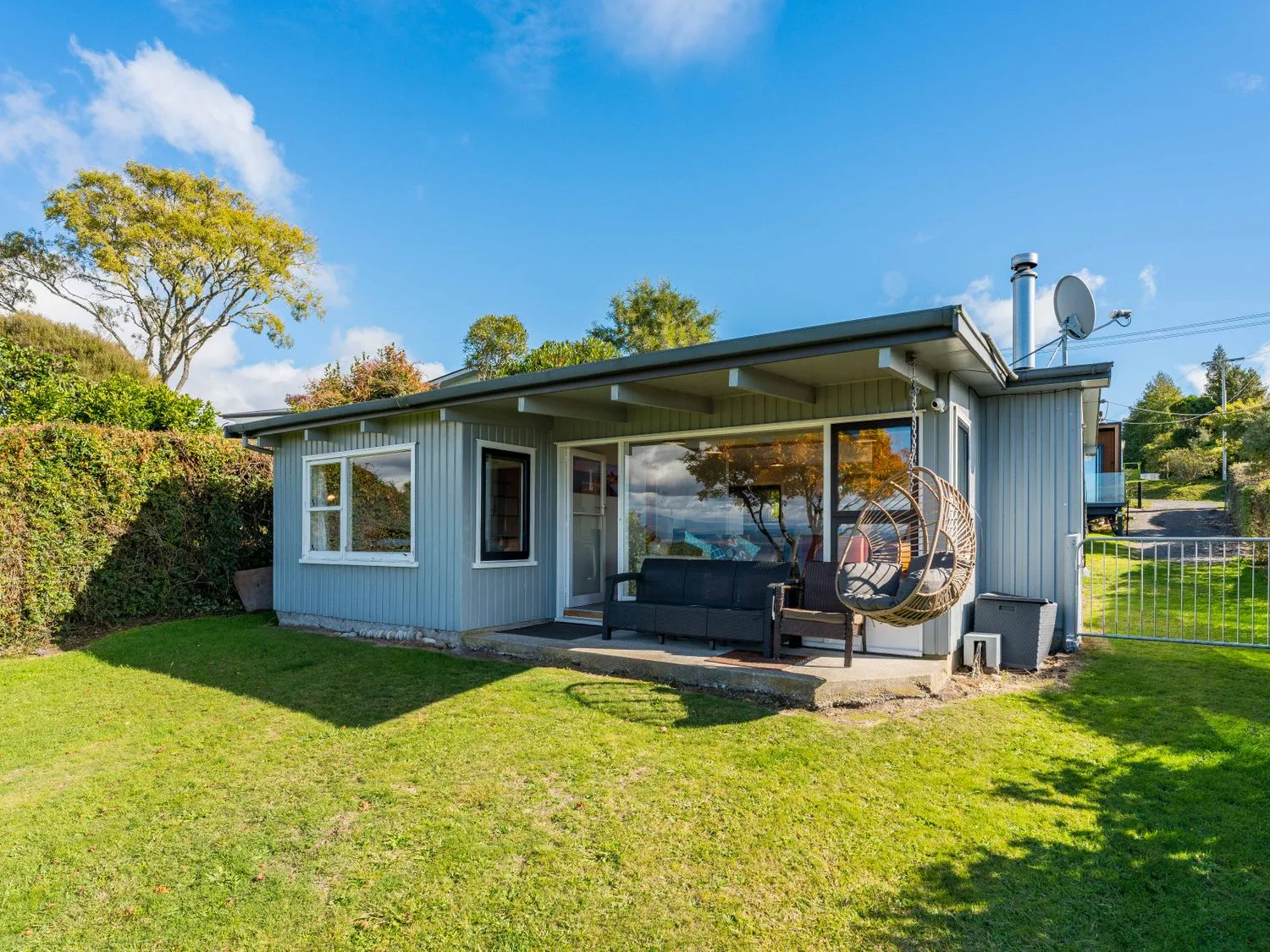 Una casa pequeña con un porche, asientos exteriores y una silla colgante sobre un césped bajo un cielo azul en Henley - Omori Holiday Home, en Omori