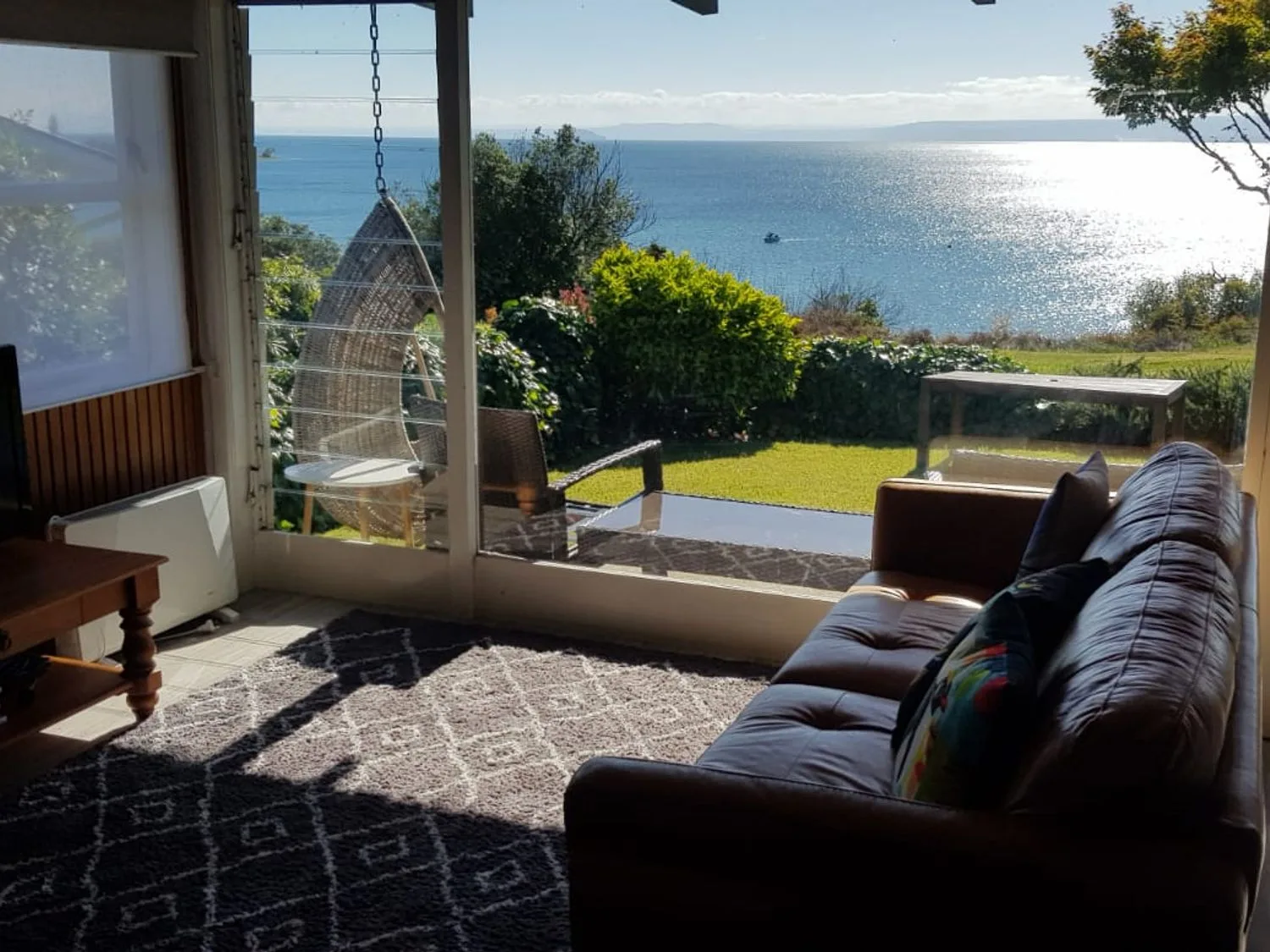 A living room with a leather sofa and a patterned rug overlooking a garden and sea at Henley - Omori Holiday Home in Omori