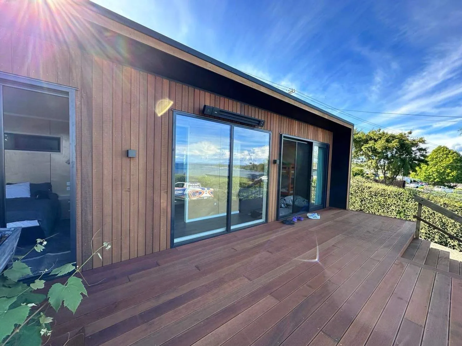 Una terraza de madera en el exterior de una casa con puertas correderas de vidrio y vistas a los árboles y al cielo en Henley - Omori Holiday Home, en Omori