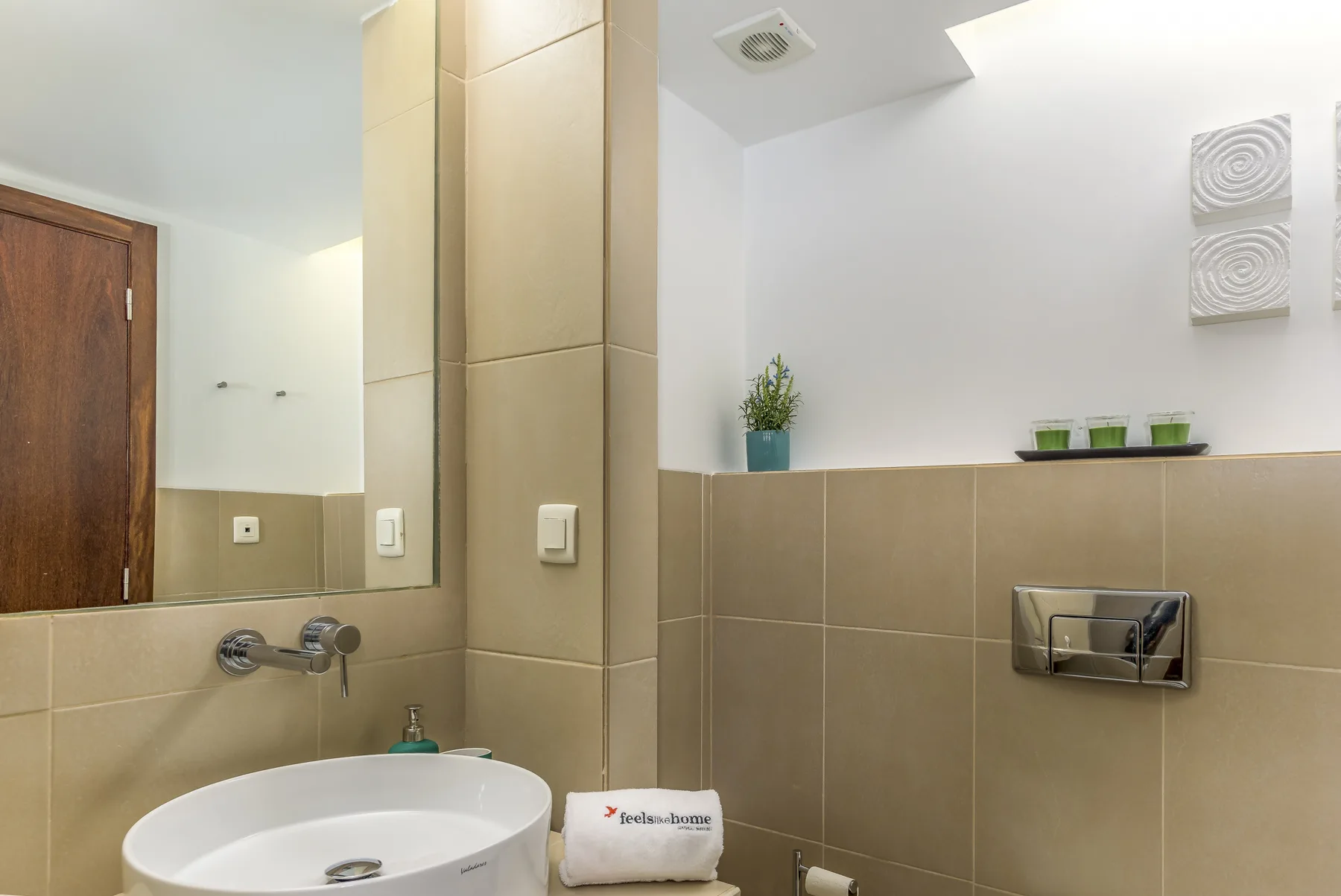 Un baño con lavabo sobre encimera, espejo de pared y paredes de azulejos.