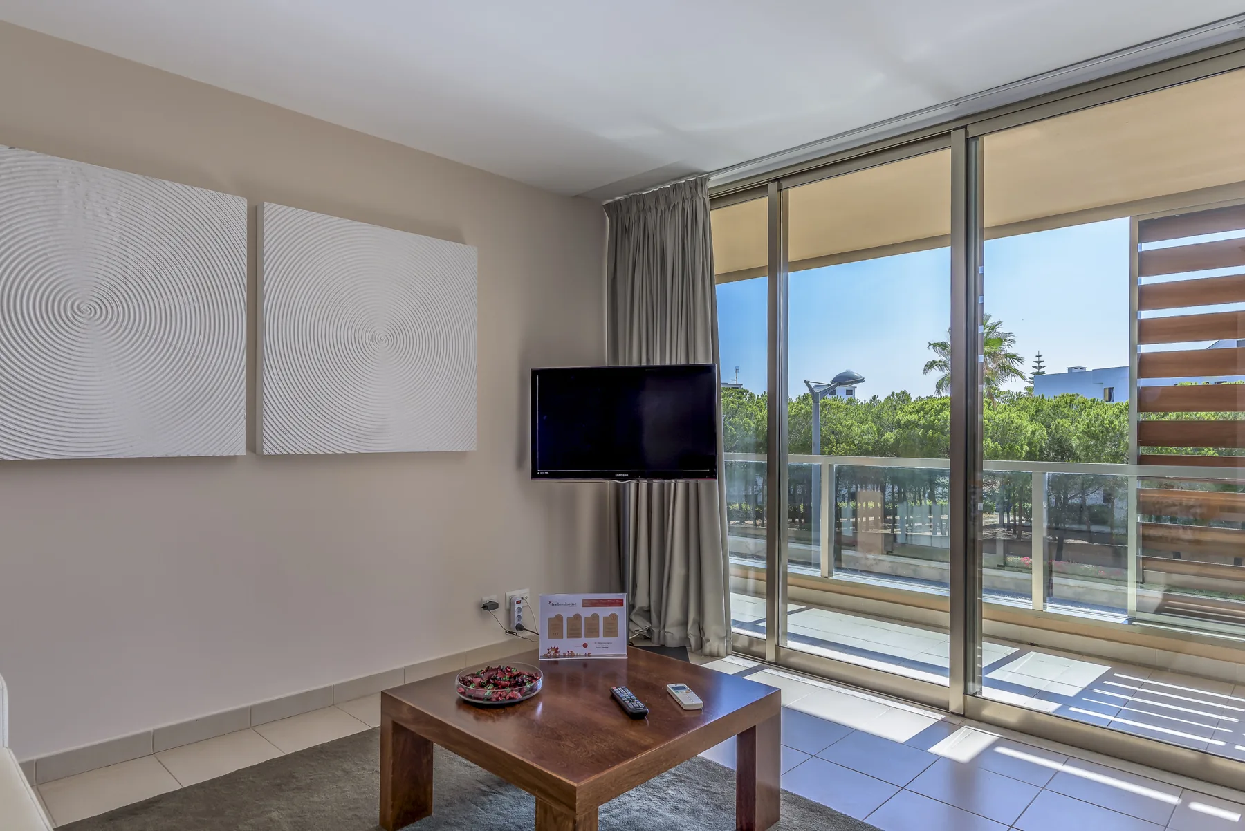 Una sala de estar con televisor, mesa de centro y puertas corredizas de vidrio hacia un balcón.
