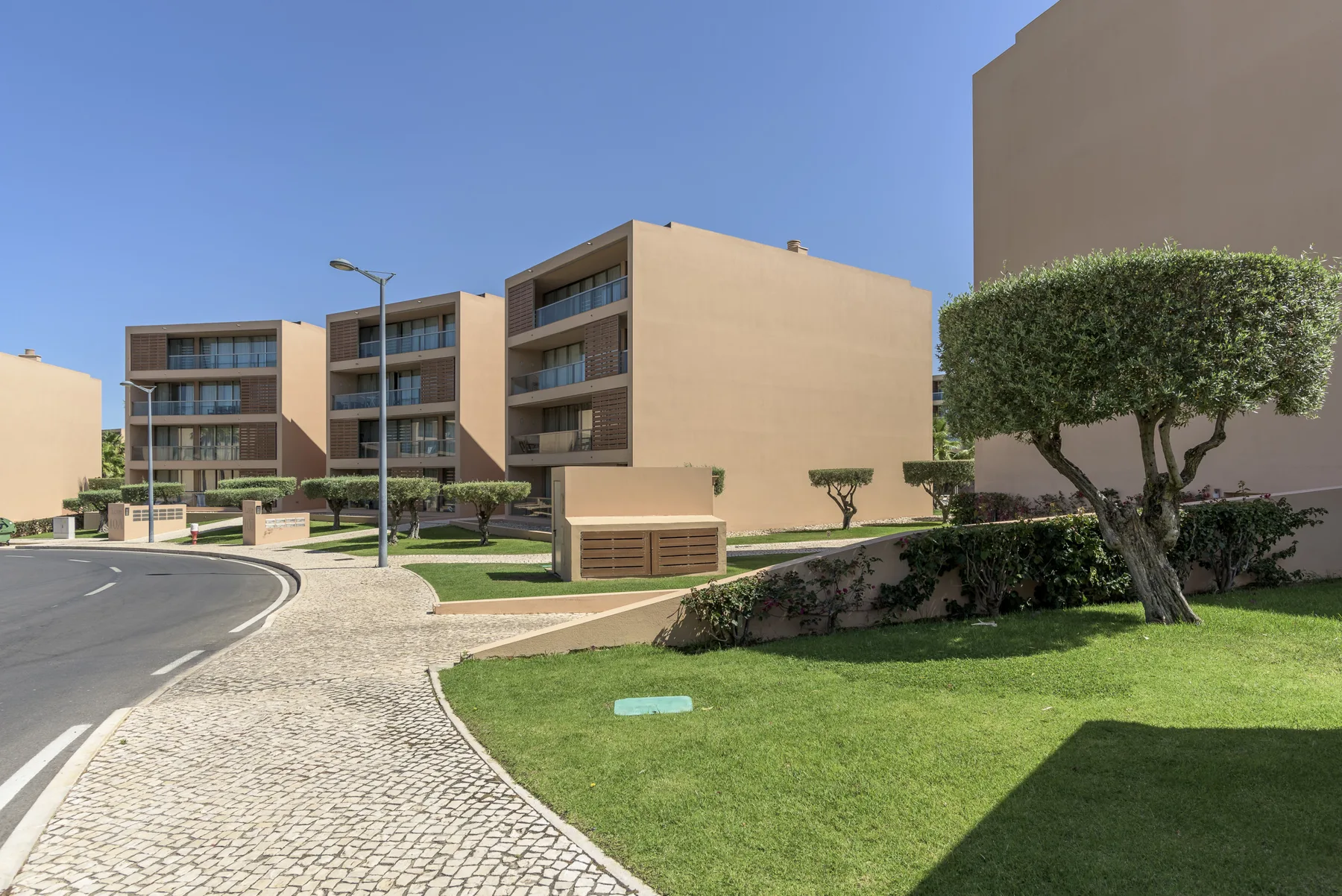 Edificios de apartamentos modernos bordean una calle curva junto a un césped ajardinado.