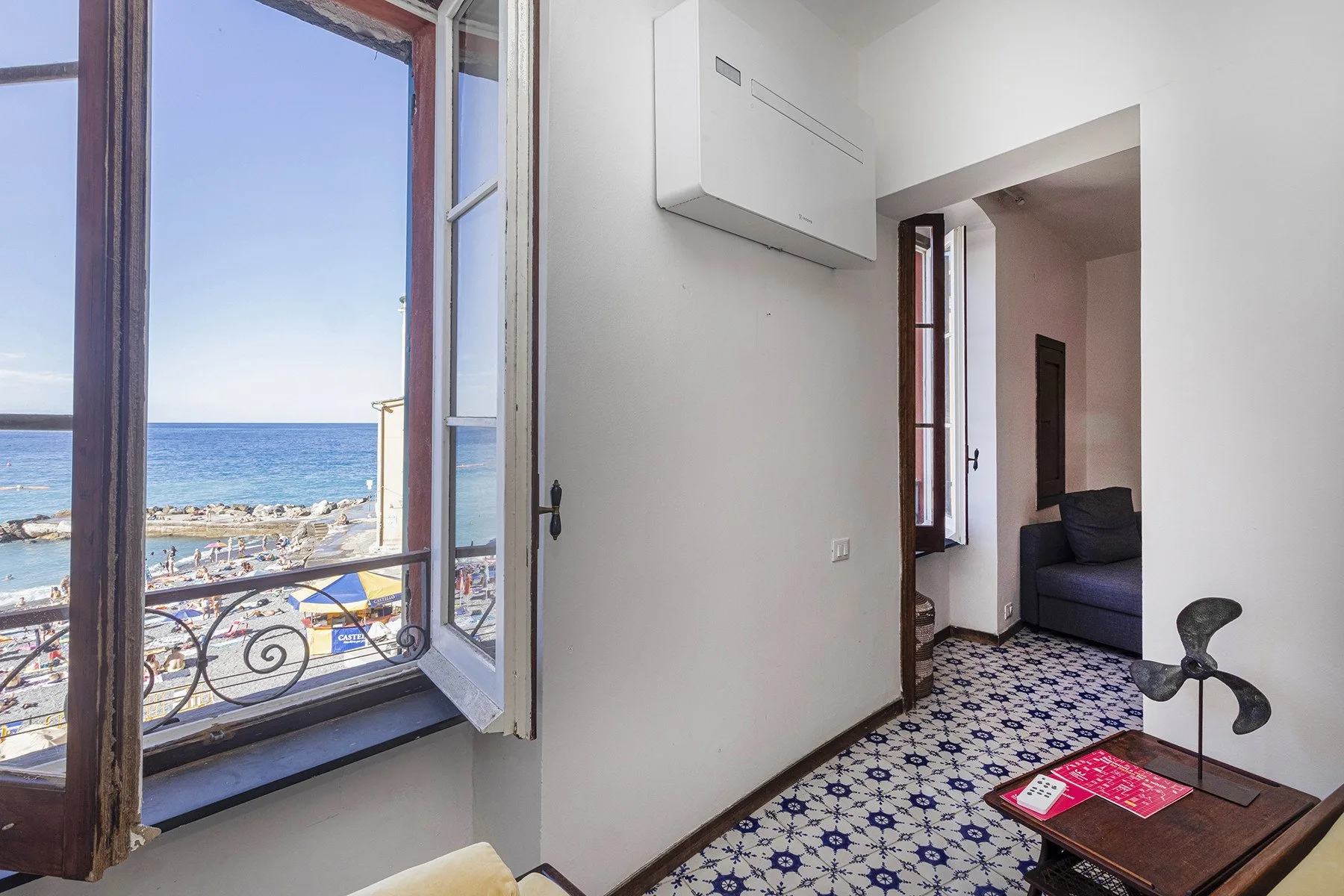 A room with an open window overlooking the sea and patterned tile flooring.