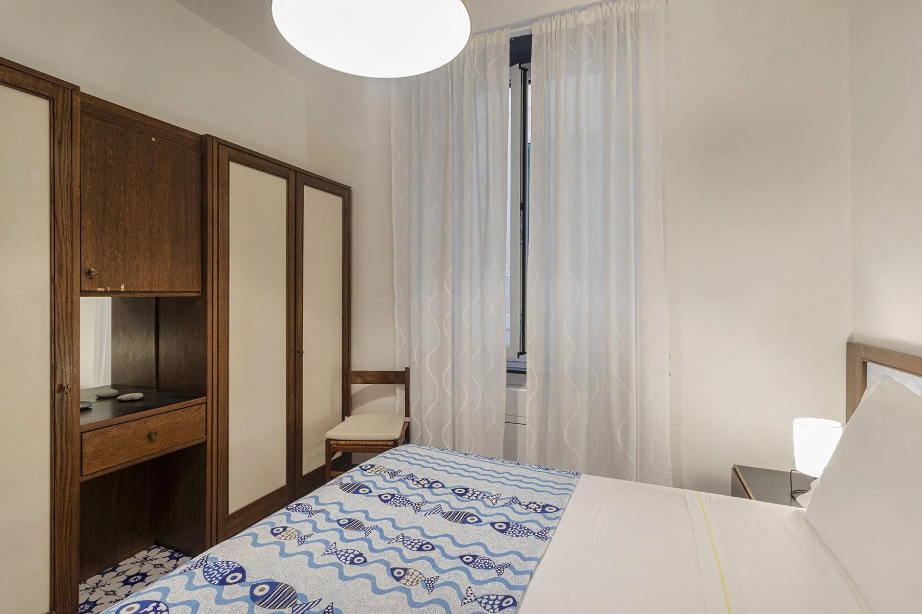 A bedroom with a bed, patterned bedding, and a tall wooden wardrobe.