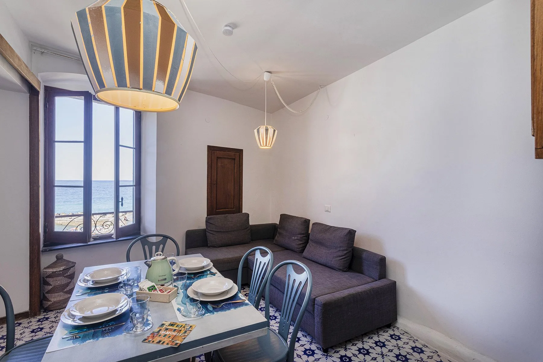 A living and dining area with a dark sofa, a set table, and tall windows.