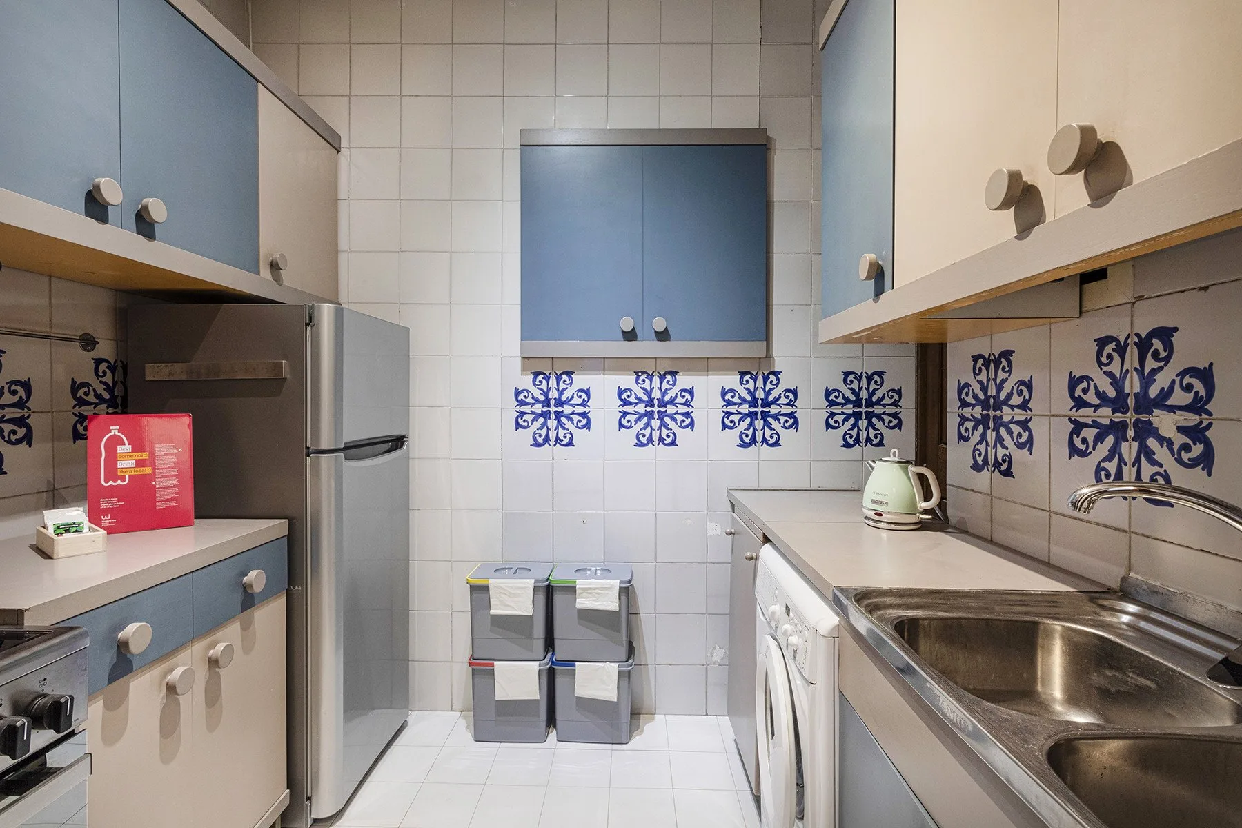 A tiled kitchen with blue-and-white cabinets, a sink, and appliances.