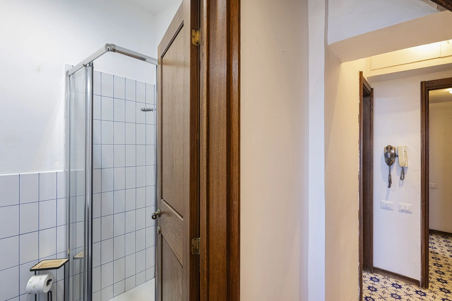 A tiled bathroom with a glass shower beside an open wooden door.