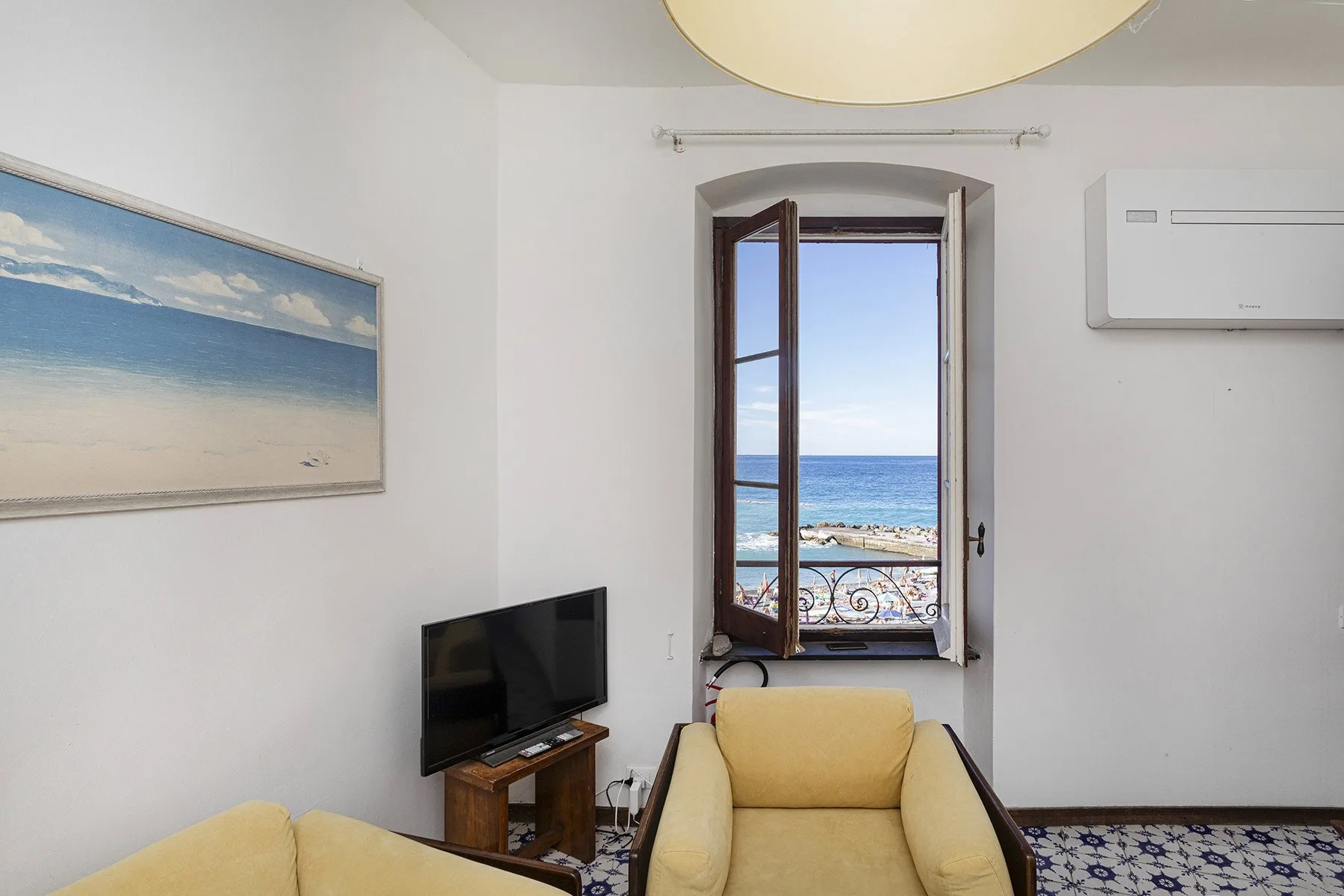 A living room with yellow seating and an open window overlooking the sea.