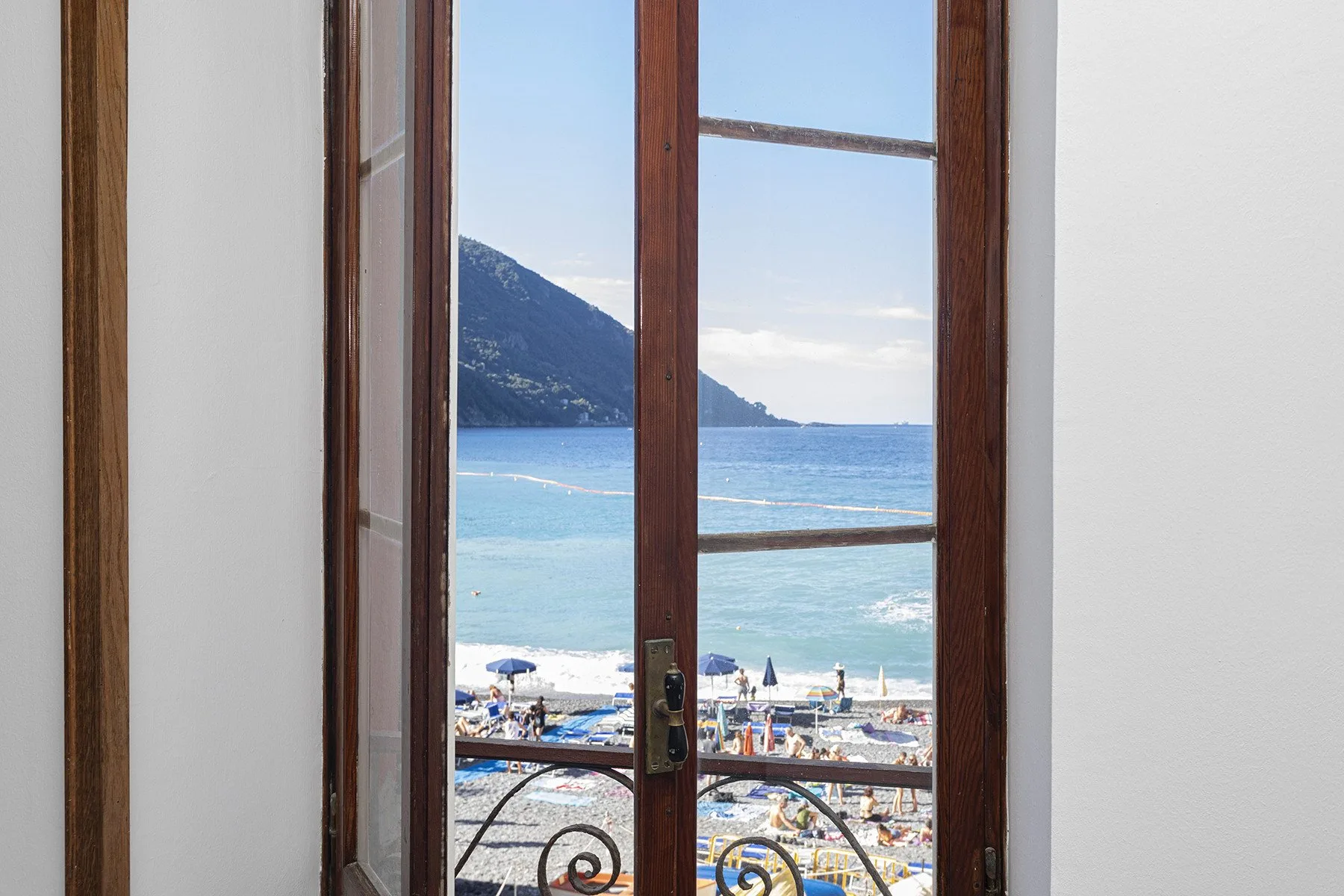A sea view through an open wooden-framed window, with a beach below.