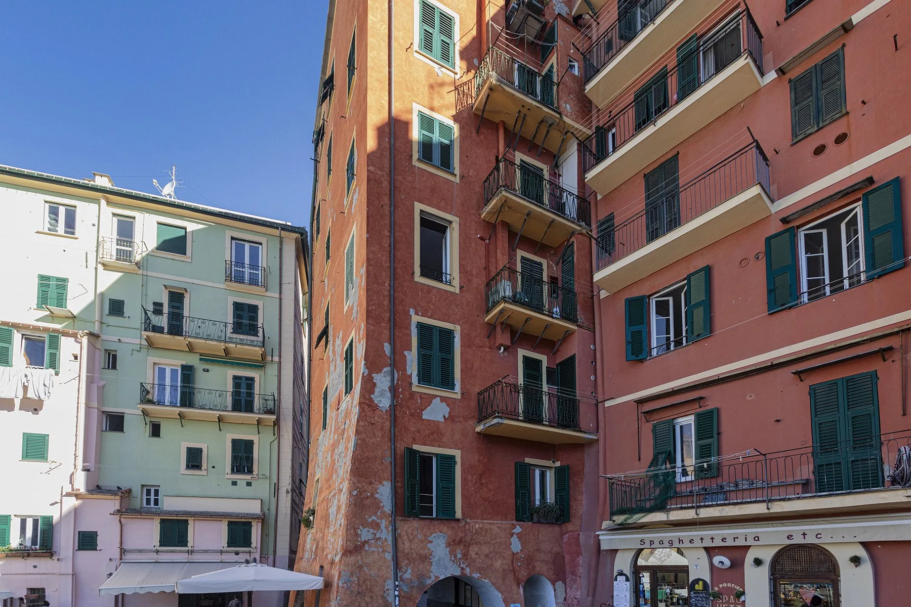 A street view of colorful apartment buildings with balconies and open shutters.