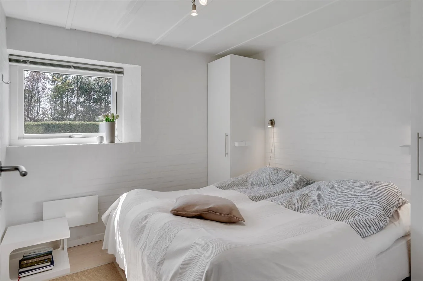 A bedroom with white bedding and a window overlooking trees.