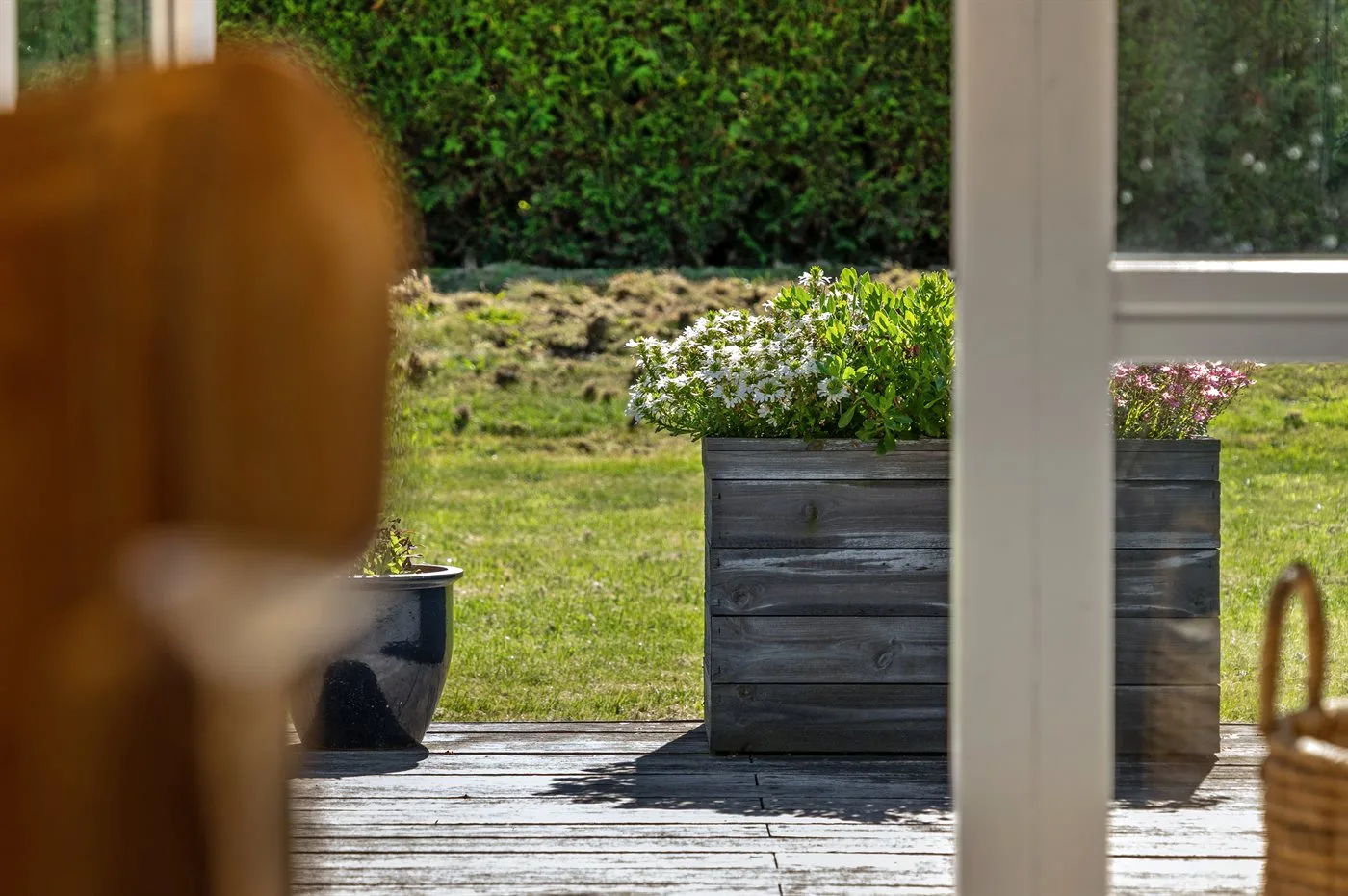 Outdoor patio with flowering planters beside a grassy garden.