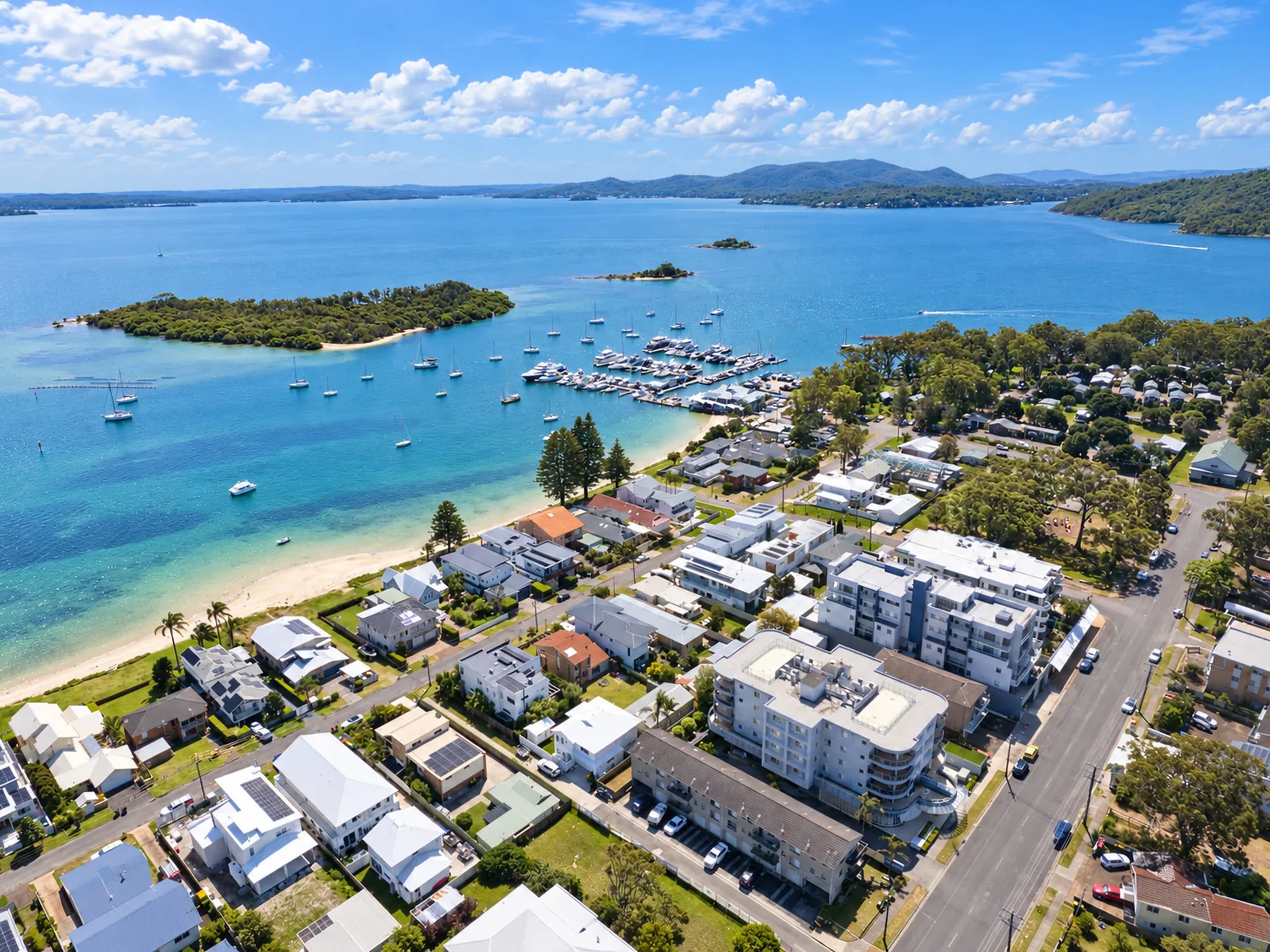 Aerial view of a coastal neighborhood beside a bay with boats and a beach.