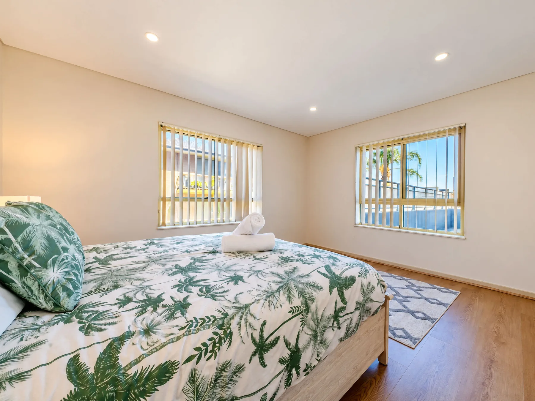 A bedroom with a leafy-patterned bedspread and windows overlooking palm trees.